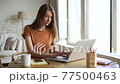 Young woman typing on laptop and having fun while sitting at table in home office. 77500463