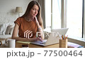 Woman working with laptop and writing while sitting at table in home office. 77500464