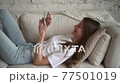 Woman using smartphone and lying on couch in apartment room indoors. 77501019