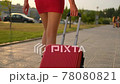 Back view of tourist traveler girl legs in red dress, high heels walking with suitcase in outdoors street city 78080821