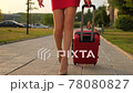 Back view of tourist woman legs in red dress, high heels walking with suitcase in outdoors street city 78080827