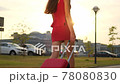 Back view of traveler girl legs in red dress, high heels walking with suitcase in sunset street city 78080830