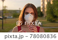 portrait of smiling happy young woman outdoors street city removing taking of protective face mask 78080836