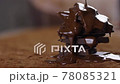 melted chocolate pouring over stack of dark chocolate at table with cocoa powder 78085321