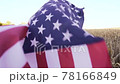 Little kid holding an American flag on the wind in a field of wheat. Summer landscape against the blue sky. 78166849