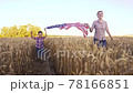 Little kid with mom holding an American flag on the wind in a field of wheat. Summer landscape against the blue sky. 78166851