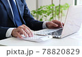 A businessman operating a calculator in front of a computer 78820829
