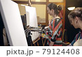 Women artists approaching the easel with paints and brushes to start painting. 79124408