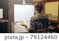Artist girl with paints and brushes walks through the workshop to the easel to start painting. 79124460