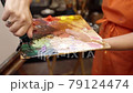Womam squeezing oil paint from a tube onto a palette. 79124474