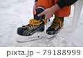 Men's hands tighten the laces on skates. Hockey skates with bright yellow laces. Preparing for skiing on snow-covered street ice. 79188999