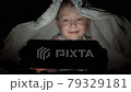 A happy boy lies in bed under a blanket and plays on mobile phone in a game in the dark. The face of the child is lit by a bright monitor. High quality 4k footage. 79329181