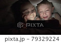 A happy boy and girl lies in bed under a blanket and plays on a phone in a game in the dark. brother and sister face of the child is lit by a bright monitor boy under the covers Computer addict child 79329224
