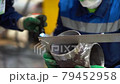 Two workers wear green gloves, protective medical mask, glasses. Man hold in hands small piece of metal pipe with stripped edges, measures size with corner ruler, checks smooth, diameter at factory.  79452958