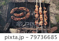 Barbeque meat and sausages or bratwurst on a grill grate in backyard. Man preparing shashlik or shish kebab over charcoal. Grilled meat on metal skewer outdoor. BBQ party or picnic food. Close up shot 79736685