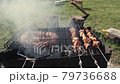 Barbeque meat and sausages or bratwurst on a grill grate in backyard. Man preparing shashlik or shish kebab over charcoal. Grilled meat on metal skewer outdoor. BBQ party or picnic food. Close up shot 79736688