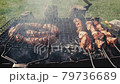 Barbeque meat and sausages or bratwurst on a grill grate in backyard. Man preparing shashlik or shish kebab over charcoal. Grilled meat on metal skewer outdoor. BBQ party or picnic food. Close up shot 79736689
