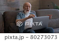 Elderly old man talk to his family via video link, smiles and gestures with his hands, emotionally shows his hands, looks at laptop screen, sitting at home. Communication with children via video chat. 80273073