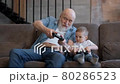 Happy family grandfather plays video game with his boy grandson at home. Mature man and boy use game joysticks. Older man wins in computer game. Happy grandfather celebrate victory. 80286523