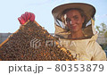 A girl beekeeper in a protective suit carries a frame with honey from a bee hive 80353879