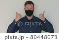 Portrait of man giving thumbs up and pointing fingers to face mask 80448073