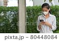 Woman wearing face mask to protect from coronavirus Covid-19 while using phone and taking selfie 80448084