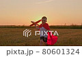 Happy smiling boy in red hero raincoat runs through summer meadow sunset of summer day with toy airplane and throws plane into flight slow motion. Kid airplane pilot. Dream concept, travel concept. 80601324