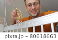 Young happy caucasian father looking at his baby in crib shaking with toy 80618663