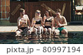 Group of friends having fun at pool. People cheers drinking summer cocktails at luxury hotel on tropical vacation. Sunny party clinking glasses with fruit cocktails near swimming pool 80997194