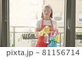 Young caucasian girl with blue napkin cleaning panoramic window at home. Washing windows with spray. 81156714
