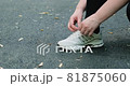 Woman ties her shoelaces on her sneakers. Process of lacing sneakers on asphalt background. 81875060