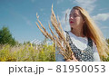 A young girl in a beautiful dress walks through a field with spikelets and wheat. 81950053