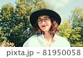 Beautiful girl with bright makeup in glasses hat. Close-up woman smiles while in the park. The wind develops hair. 81950058