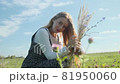 A young girl in a beautiful dress walks through a field with spikelets and wheat. 81950060
