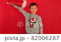 Boy in a New Year's cap and sweater on a red background. Child waiting for Christmas. Happy boy getting ready for the new year. 82006287