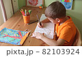 Boy drawing tree sitting bu desk 82103924