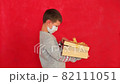 Boy in a New Year's sweater on a red background. Child with a gift in hands in anticipation of Christmas. Young boy getting ready for the new year. Video of a child with a New Year's surprise 82111051