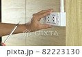 Electrician is using a screwdriver to install a power outlet on a wooden wall. 82223130