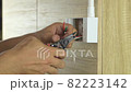 Electrician is stripping electrical wires in a plastic box on a wooden wall to install the electrical outlet. 82223142