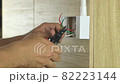 Electrician is stripping electrical wires in a plastic box on a wooden wall to install the electrical outlet. 82223144