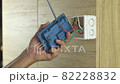Electrician is using a screwdriver to tighten the wires to the electrical plug on a wooden wall. 82228832