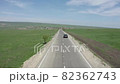 A black car drives along the road among the green fields towards a small town, aerial view 82362743