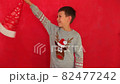 Boy in a New Year's cap and sweater on a red background. Child waiting for Christmas. Happy boy getting ready for the new year. 82477242