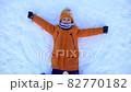 A young boy in a yellow jacket lies in the snow and makes a snow angel with his arms and legs. Child in the snow in winter. Winter outdoor games 82770182