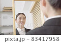 外出前に鏡を見て身支度をするスーツ姿の若い女性 83417958