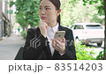 街中でスマホを見ながら周囲を確認するスーツ姿の若い女性 83514203