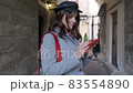 Young beautiful girl in autumn dress uses a smartphone. Beautiful woman walks through the old city with a smartphone in her hands  83554890