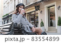 Young beautiful girl drinking coffee on the street sitting on a bench. The girl enjoys morning coffee before work 83554899