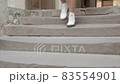 A woman quickly descends an old stone staircase in autumn white shoes. Female legs close-up 83554901
