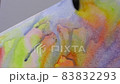The artist paints an abstract figure on a white canvas with watercolor paints. 83832293